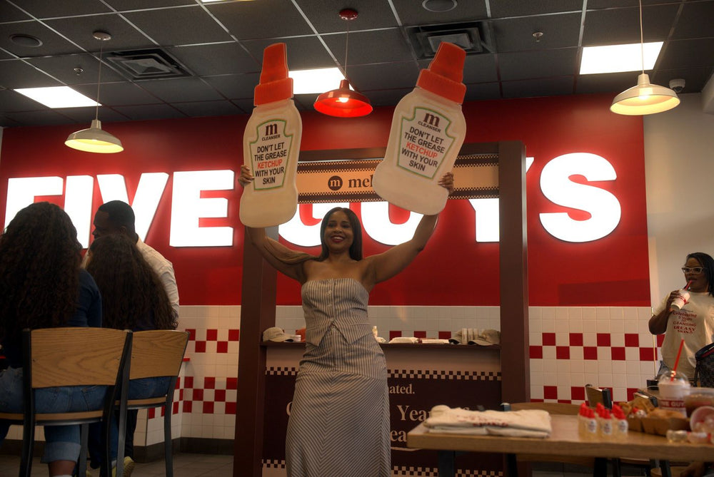 Guest posing with two giant cleanser bottles in front of the Five Guys wall