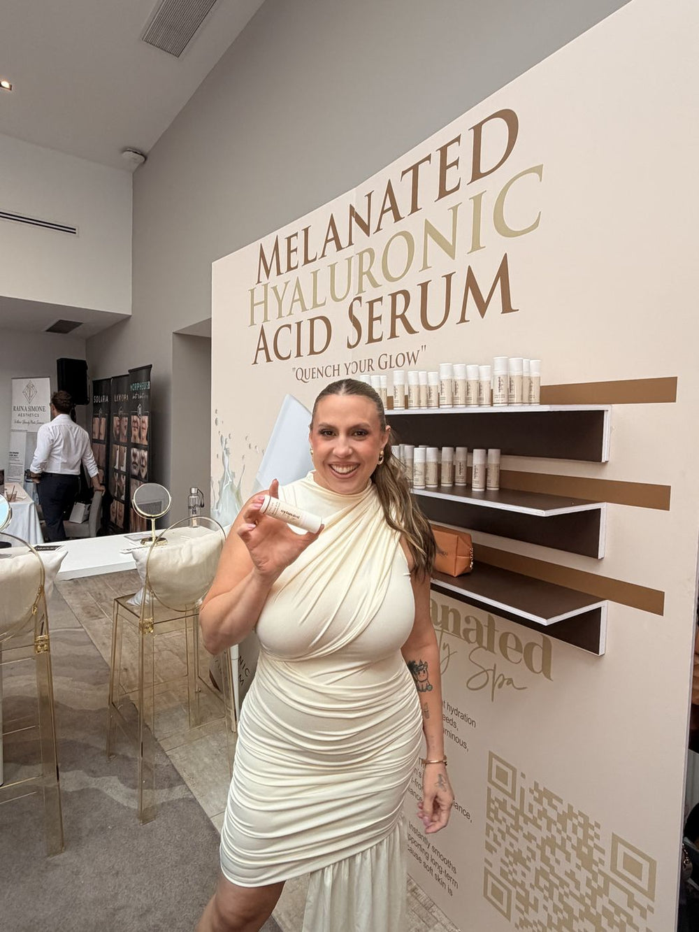 Guest in a white draped dress at the Hyaluronic Acid Serum wall